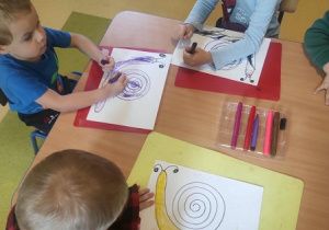 Dzieci kolorują przy stoliku ślimaki.