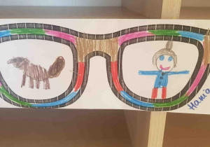 W odbiciu narysowanych okularów widać dziewczynkę z pieskiem