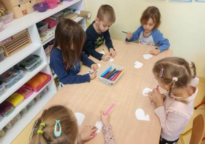 Dzieci siedzą przy stoliku i projektują przy użyciu mazaków rękawiczki dla bałwanka