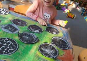 Dziewczynka wskazuje bombkę swojego autorstwa na wspólnym plakacie przedstawiającym choinkę