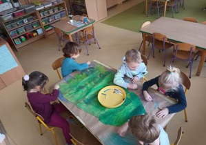 Grupa dzieci współpracuje przy stoliku i koloruje poszczególne elementy szablonu choinki