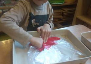 Chłopiec rozprowadza za pomocą dłoni białą i czerwoną farbę w koszulce na dokumenty