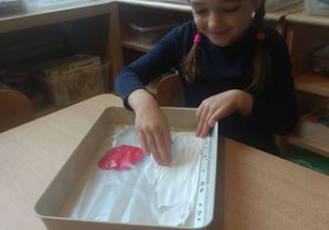 Nela bierze udział w zabawie sensorycznej i rozprowadza dłońmi farbę w kolorze białym oraz czerwonym