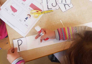 Dziewczynka układa napis Polska z powycinanych liter
