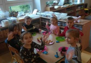 Dzieci siedzą przy stoliku i jedzą urodzinowy poczęstunek