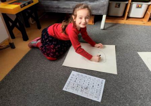 Dziewczynka gra w grę "Wylosuj twarz" i rysuje wyniki na dużym arkuszu przy pomocy flamastra