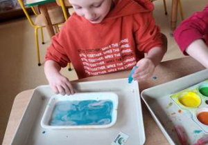 Chłopiec maluje na mleku kompozycję wykorzystując niebieską farbę