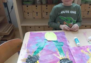 Franio siedzi przy stoliku i prezentuje ukończoną przez siebie pracę plastyczną zainspirowaną obrazem Van Gogha "Słoneczniki"