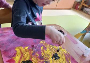Dziewczynka stempluje środek namalowanego słonecznika patyczkiem kosmetycznym zamoczonym w czarnej temperze