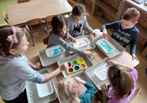 Dzieci siedzą przy stoliku i malują na mleku kompozycje według własnej inwencji twórczej z wykorzystaniem różnych kolorów farb