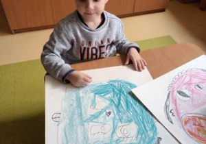 Chłopiec koloruje pastelami narysowany przez siebie portret