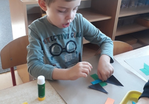 chłopiec przykleja kształty geometryczne tworząc swoją kompozycję