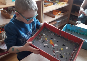 chłopiec porusza pudełkiem ze szklanymi kulkami umoczonymi w farbie