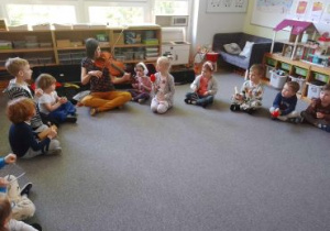 Dzieci siedzą w kręgu na dywanie i wsłuchują się w dźwięk skrzypiec