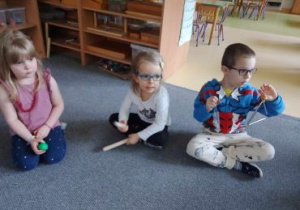 Dzieci siedzą na dywanie i grają na instrumentach