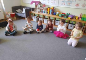 Dzieci siedzą w kręgu na dywanie i grają na instrumentach muzycznych