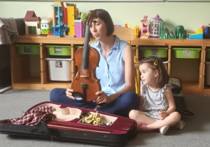 Dziewczynka wraz z mamą prezentuje skrzypce podczas warsztatu muzycznego