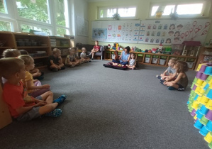 Dzieci siedzą na dywanie w czasie warsztatów muzycznych i słuchają informacji dotyczących budowy skrzypiec