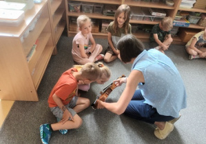 Mama Niny pokazuje dzieciom siedzącym w kręgu skrzypce