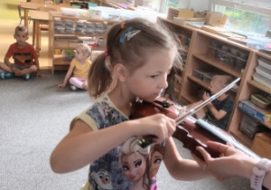 Dziewczynka trzyma w dłoniach smyczek i próbuje samodzielnie grać na skrzypcach