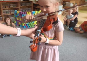 Dziewczynka trzyma w dłoniach skrzypce i podejmuje próby gry