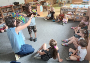 Dzieci siedzą w kręgu w czasie warsztatu muzycznego, Julek w środku kręgu podejmuje próby grania na skrzypcach